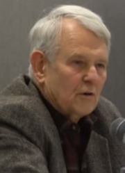 Head shot of white-haired, serious-looking male.