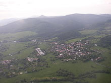 Letecký pohled na část Lužických hor; v popředí Jiřetín pod Jedlovou obklopený lukami, v pozadí zalesněná krajina: zleva Weberberg, údolí Milířky, Luž a Pěnkavčí vrch