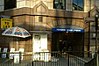 A beige-bricked building with a rectangular, dark blue sign reading "MANSION HOUSE STATION" in white letters and a yellow sign reading "OFFICES TO LET"