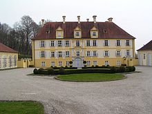 Vue d'un grand bâtiment à la façade jaune, derrière une large cour.