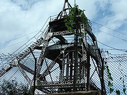 Metal superstructure of a mine shaft, seen through a fence at ground level