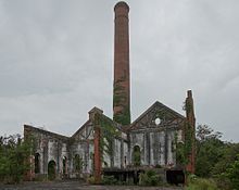 Ruined buildings in front of a chimney which is slowly being consumed by vines