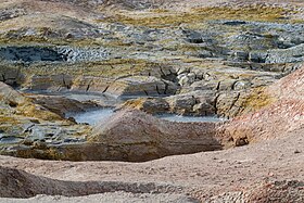 A pool of greyish-blue bubbling sludge surrounded by rocks and steam