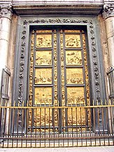 A pair of large bronze doors, with ornate frames. The doors are divided into ten rectangular sections with decorations between them. Each section contains a relief sculpture telling a story from the Old Testament. The panels and parts of the frames are covered with gold.