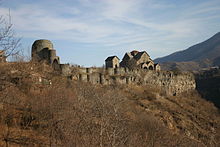 Ancient stone church with many gables sits in a grassy area that is surround by vegetation.