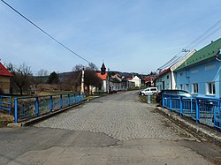 Střed obce s mostem přes potok Olšinku a kaplí svaté Anny