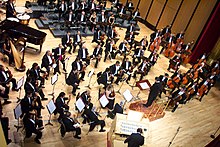 Orchestre philharmonique, plusieurs personnes habillées de noir, assises, tenant un instrument.