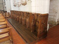 Vue de sept stalles en bois alignées contre le mur intérieur d'une église.