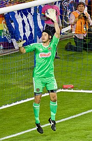 Goalkeeper John McCarthy in a green Philadelphia Union jersey, jumps while in front of an empty goal with his left arm raised.