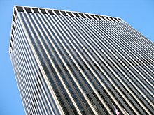 Street view of top half of skyscraper against the sky; its outside is dominated by vertical black and white lines