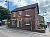 A rectangular, red-brick building, seen from the north-west, at the corner of two streets. Signs on the two visible walls read "Butson & Blofeld".