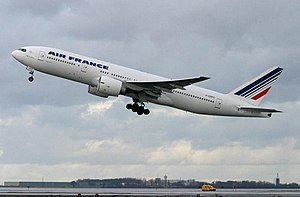 Front quarter view of the first 777 built in flight wearing Cathay Pacific livery and with flaps partially extended and landing gear retracted.