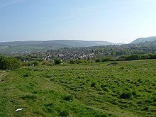 Across the overgrown site of the fort where no walls remain with the hills of Tintwistle and Peak Naze behind