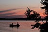 Two silhouetted people fishing on a boat