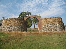 Photographie en couleur d'un monument en ruines, deux tours et une porte apparaissent