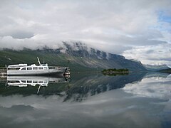 Un bateau sur un lac entouré de montagnes, sous un ciel nuageux.