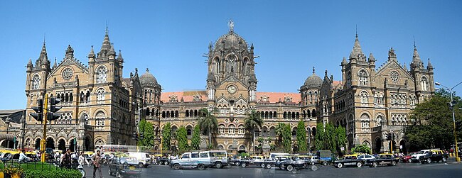 A brown building with clock towers, domes and pyramidal tops. Also a busiest railway station in India.[28] A wide street in front of it