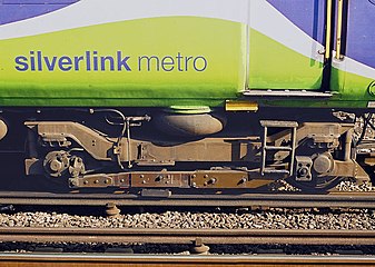 With surface contact third and fourth rail systems a heavy "shoe" suspended from a wooden beam attached to the bogies collects power by sliding over the top surface of the electric rail. This view shows a British Rail Class 313 train.