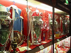 Four trophies inside a glass cabinet. The trophies have ribbons on them and there is memorabilia next to them