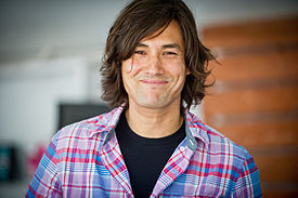 David Usher wearing a black t-shirt underneath a light checkered shirt, smiling at camera