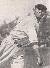 Eiji Sawamaru in baseball hat and uniform, with his arm hanging down in front of him