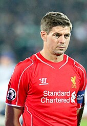 The head and torso of a man with short, brown hair. He is wearing a red shirt and a black armband.