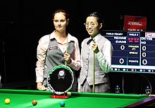 Two women holding snooker cues, standing at a snooker table