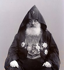 Photographie d'un homme à la barbe blanche, assis et portant une tenue cléricale arménienne.