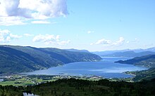 Foto eines Fjords in bergiger Umgebung. Am inneren Ende des Fjords befinden sich einige Gebäude