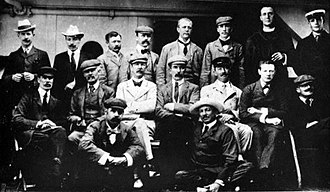 A formative photograph of 17 men. Eight stand, seven sit on chairs and two are on the floor.