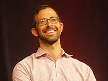 Person with glasses in front of a dark background