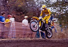 Motard habillé de jaune sur une moto jaune, en plein saut durant une course de moto-cross.