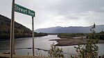 A wide river flows through hills. A sign in the foreground says "Stewart River".