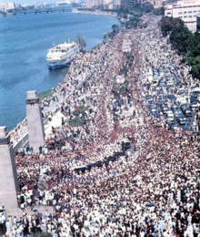 Photographie en plongée d'une immense foule dans une avenue longeant un fleuve.