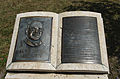 Photographie d'un monument en forme d'un livre, à gauche le dessein d'un homme portant des lunettes, à droite une page avec un texte.