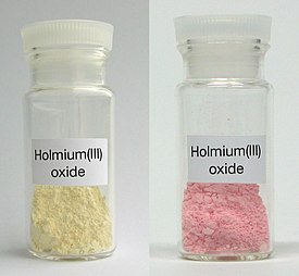 Holmium(III)oksidia päivänvalossa (vasemmalla) ja trikromaattisessa valossa (oikealla)