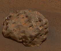 Figure 8. An example iron-nickel meteorite, Heat Shield Rock, with many hematite spherules in the background. Heat Shield Rock can also be seen in Figure 3 as a small dot about 20 m to the left of the discarded heat shield (hence the meteorite's name). It is large. Its longest dimension is 31 cm,[43] i.e. roughly basketball-sized. Large iron-nickel meteorites were occasional featured finds by Opportunity, the rover found six of them. Image taken on Sol 346 (2005-02-01).