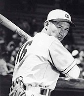 Tetsuharu Kawakami in baseball hat and uniform, holding a bat and in a batting stance in front of a stadium crowd