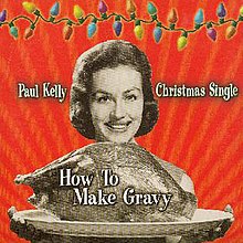 A sepia coloured image of a woman presenting a platter containing a large roast bird (possibly a turkey). Her smiling face is visible beyond the bird, her fingers appear below the platter. The background is red. A strand of coloured Christmas lights stretches across the top of the image. The artist's name is located to the left of the woman's head and the words, Christmas Single, are to her right. The title of the single is written over the image of the roast bird.